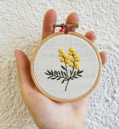 a hand holding a small embroidered yellow flower