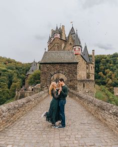 a man and woman standing on a bridge in front of a castle