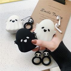 a hand holding an airpods case with ghost faces on it and other accessories around it