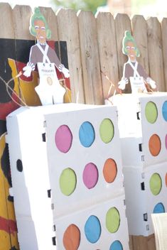 several boxes with different colored dots on them sitting in front of a wooden fence and paper cutouts