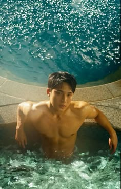 a shirtless man sitting in the water next to a swimming pool