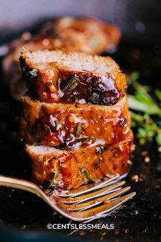 two slices of meat on a plate with a fork next to it and herbs in the background