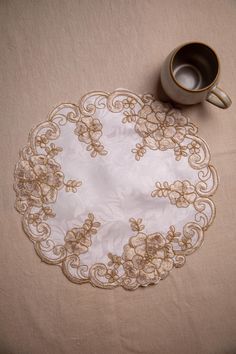 a coffee cup sits next to a lace doily on a tablecloth with an ornate design