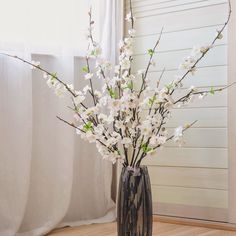 a vase filled with white flowers sitting on top of a wooden floor next to a window