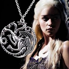 a woman with long blonde hair wearing a silver necklace and holding a dragon pendant in front of her face