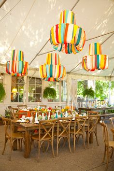 a large tent with tables, chairs and hanging lights in the ceiling is decorated with multicolored paper lanterns