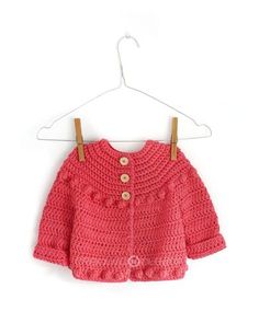 a pink crocheted sweater hanging on a hanger with clothes pins attached to it