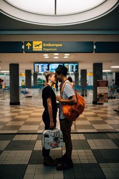 a man and woman standing in an airport with their suitcases on the ground, kissing