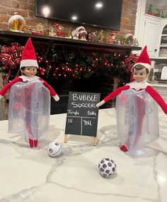 two elfs sitting on top of a table next to a sign and soccer ball