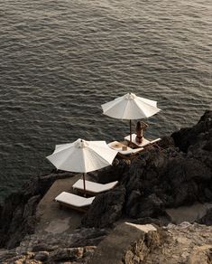 three umbrellas are set up on the edge of a cliff by the ocean with people sitting under them