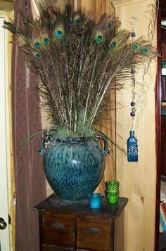 peacock feathers are in a blue vase on a small table next to a brown cabinet