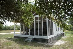 a small white house sitting on top of a grass covered field next to a tree