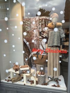 a window display with snow falling on the ground and christmas decorations in front of it