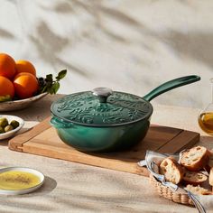 a green cast iron skillet sitting on top of a wooden cutting board next to oranges