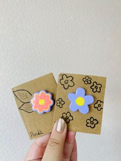 two handmade flower magnets sitting on top of a piece of brown paper next to each other