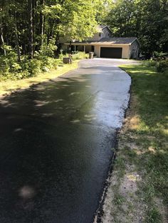 an empty driveway in front of a house surrounded by trees and grass on a sunny day