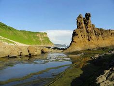 some very pretty rocks by the water with green grass on top and blue sky in the background