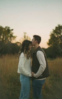 a man and woman standing next to each other in a field with tall grass at sunset