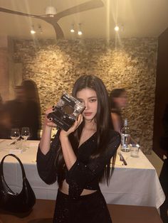 a woman holding up a camera in front of her face at a table with wine glasses on it