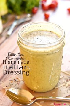 a jar filled with homemade italian dressing on top of a wooden table next to a spoon