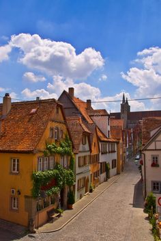 an old european street lined with houses under a blue sky filled with white fluffy clouds