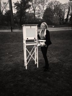 a woman standing next to a sign in the grass with trees in the back ground