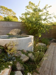 an outdoor hot tub surrounded by rocks and greenery next to a wooden deck area