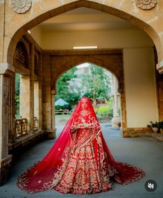 a woman in a red and gold bridal gown stands under an archway with her veil draped over her head