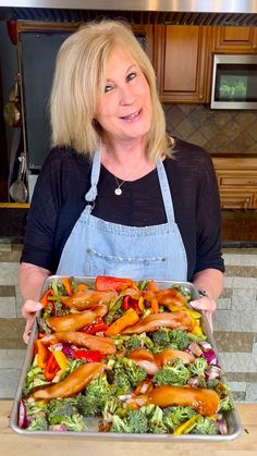 a woman in an apron holding a tray with vegetables and meats on the side