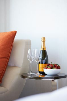 a table with two wine glasses and a bowl of strawberries on it next to a bottle of champagne