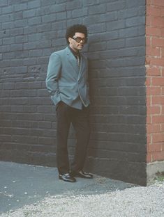 a man in a suit leaning against a brick wall