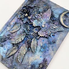 an art journal with blue and silver designs on it's cover, sitting on top of a white surface