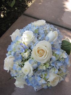 a bouquet of white roses and blue hydrangeas sits on the sidewalk outside in front of some bushes