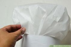 a hand holding a white paper bag over a toilet paper roll that is wrapped in plastic