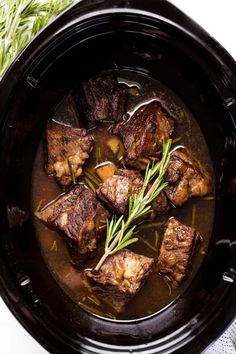 beef stew in a black bowl with rosemary garnish on the side and fresh herbs