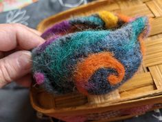 a person is holding a needle - felted animal in a basket with yarn on it