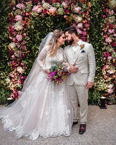 a man and woman standing next to each other in front of a flower covered wall