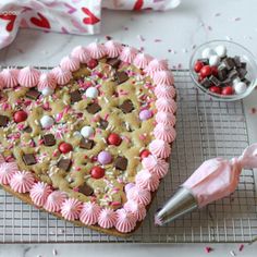 a heart shaped cookie with pink icing and sprinkles on a cooling rack