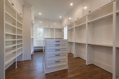 an empty walk in closet with white shelving and drawers on the wall, along with wooden floors