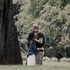 two people standing next to each other near a tree