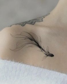 a woman's chest with a black feather tattoo on her left shoulder and right breast