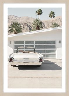 an old white car parked in front of a garage with palm trees and mountains behind it