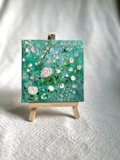 a small easel with flowers painted on it sitting on a white cloth covered surface