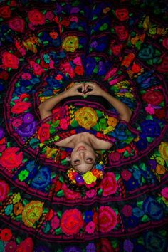 a woman laying on top of a colorful rug covered in crocheted flowers and leaves