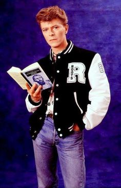 a man is holding a book and posing for a photo in front of a blue background