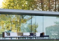 an outdoor lounge area with glass walls and trees in the background