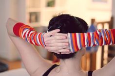 a woman is holding her hands over her head and covering her face with striped gloves