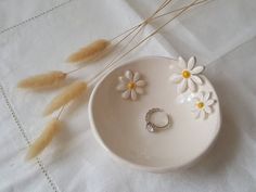 a white bowl with daisies and two rings on it