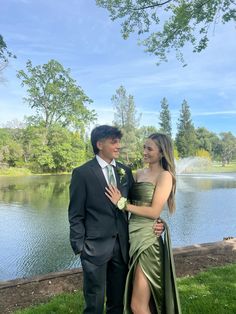 a young man and woman standing next to each other in front of a body of water