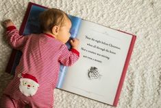 a baby laying on the floor next to a book with an image of santa claus